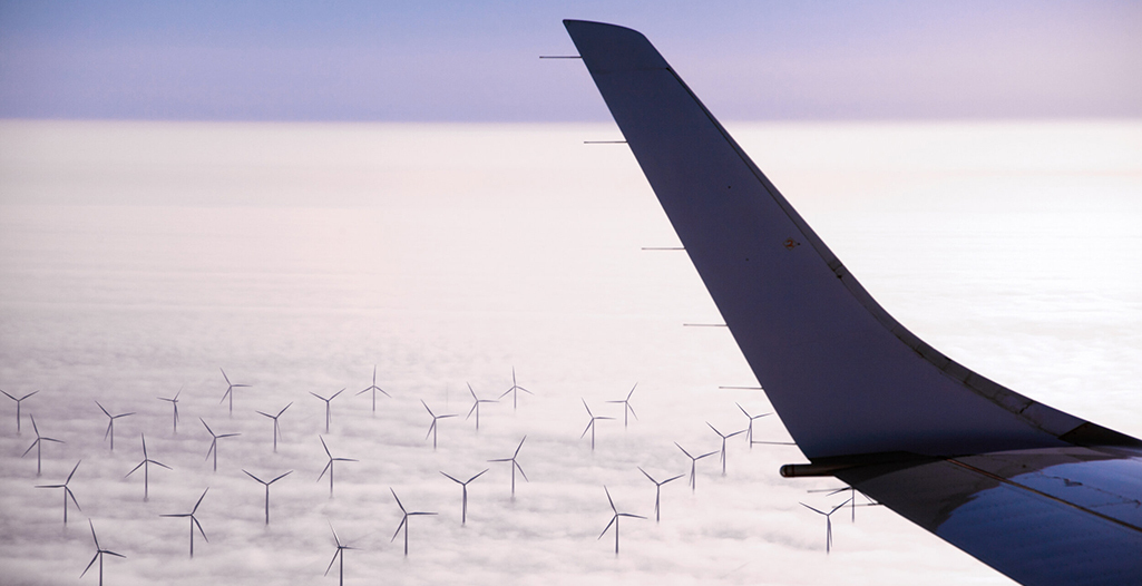 Aircraft flying over windmill park between coming through the clouds