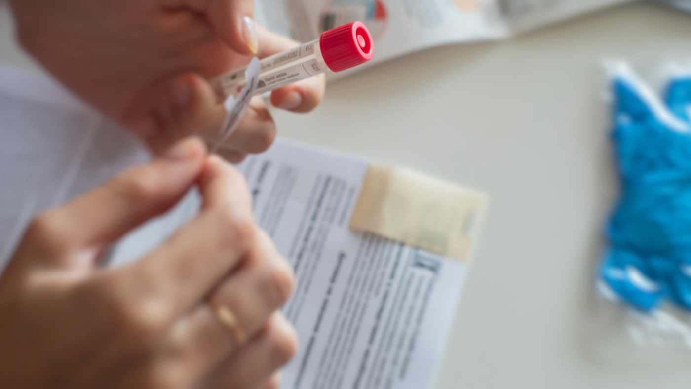 Close-up of hands holding a venous blood collection tube with instructions and medical supplies in the background.