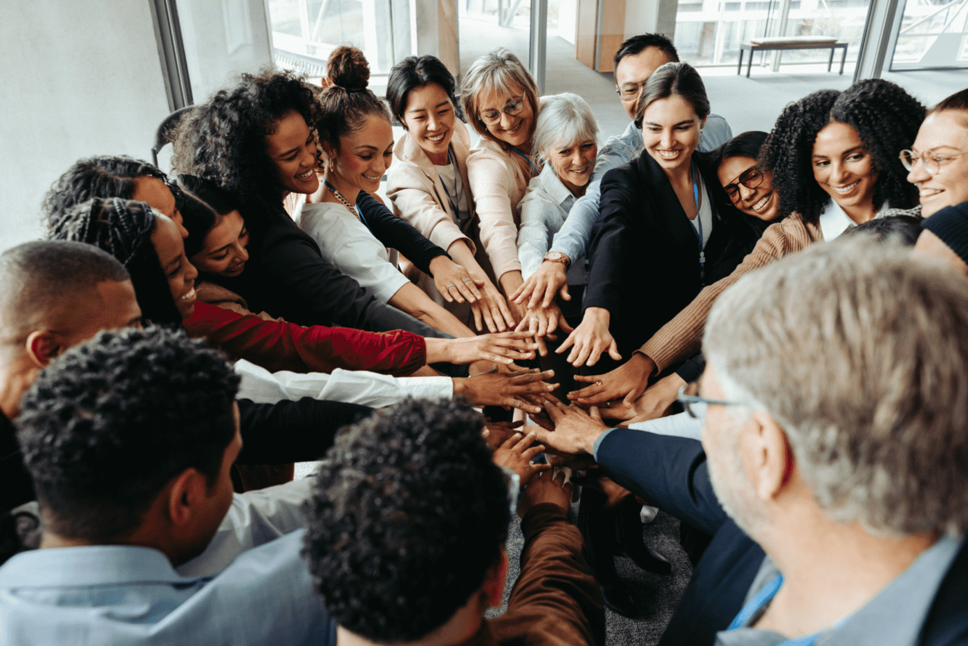 A diverse group of employees standing in a circle with their hands together in the center, symbolizing teamwork and unity in a corporate environment.
