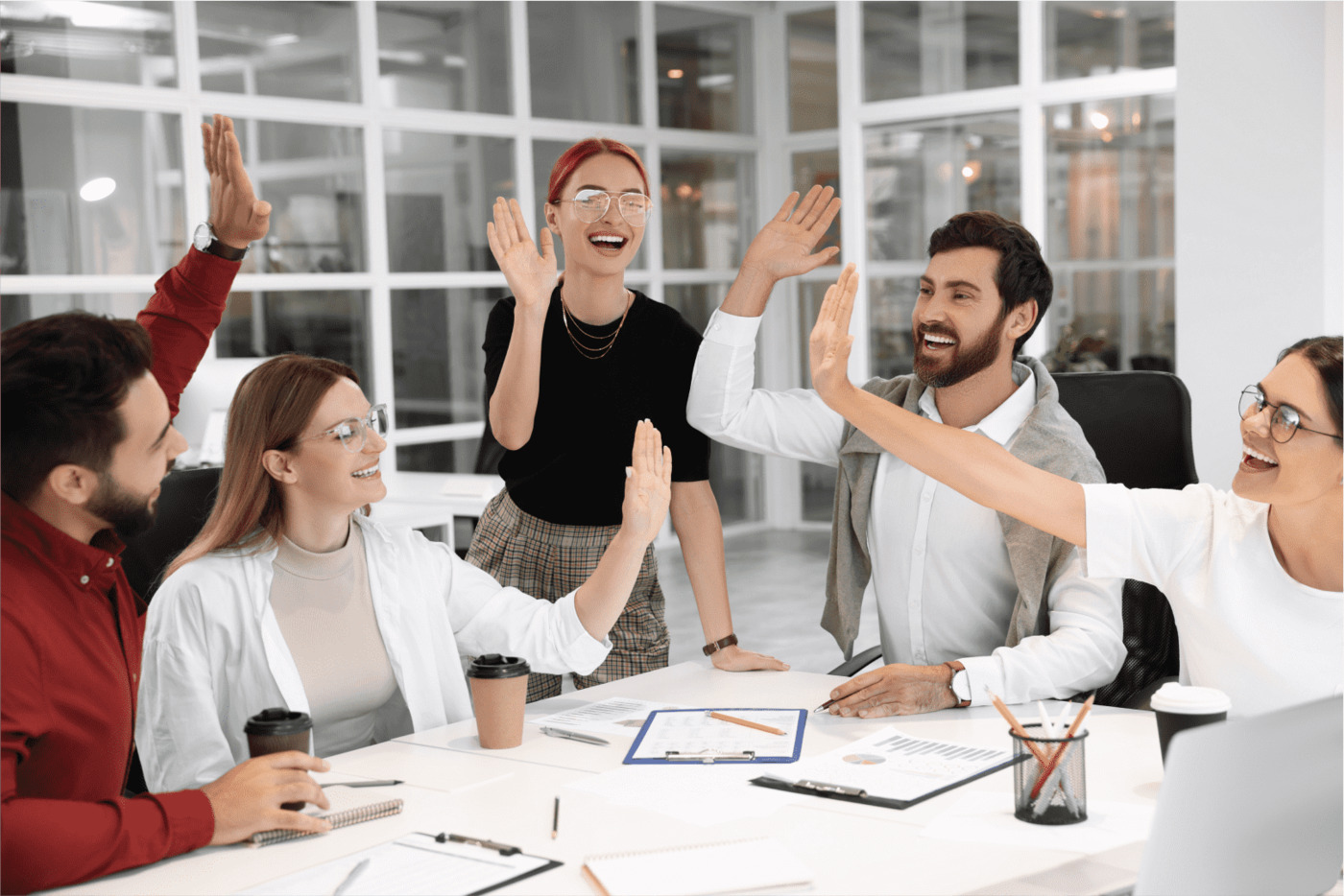A group of cheerful executives in a modern office giving each other high fives, symbolizing teamwork, success, and a positive work environment.