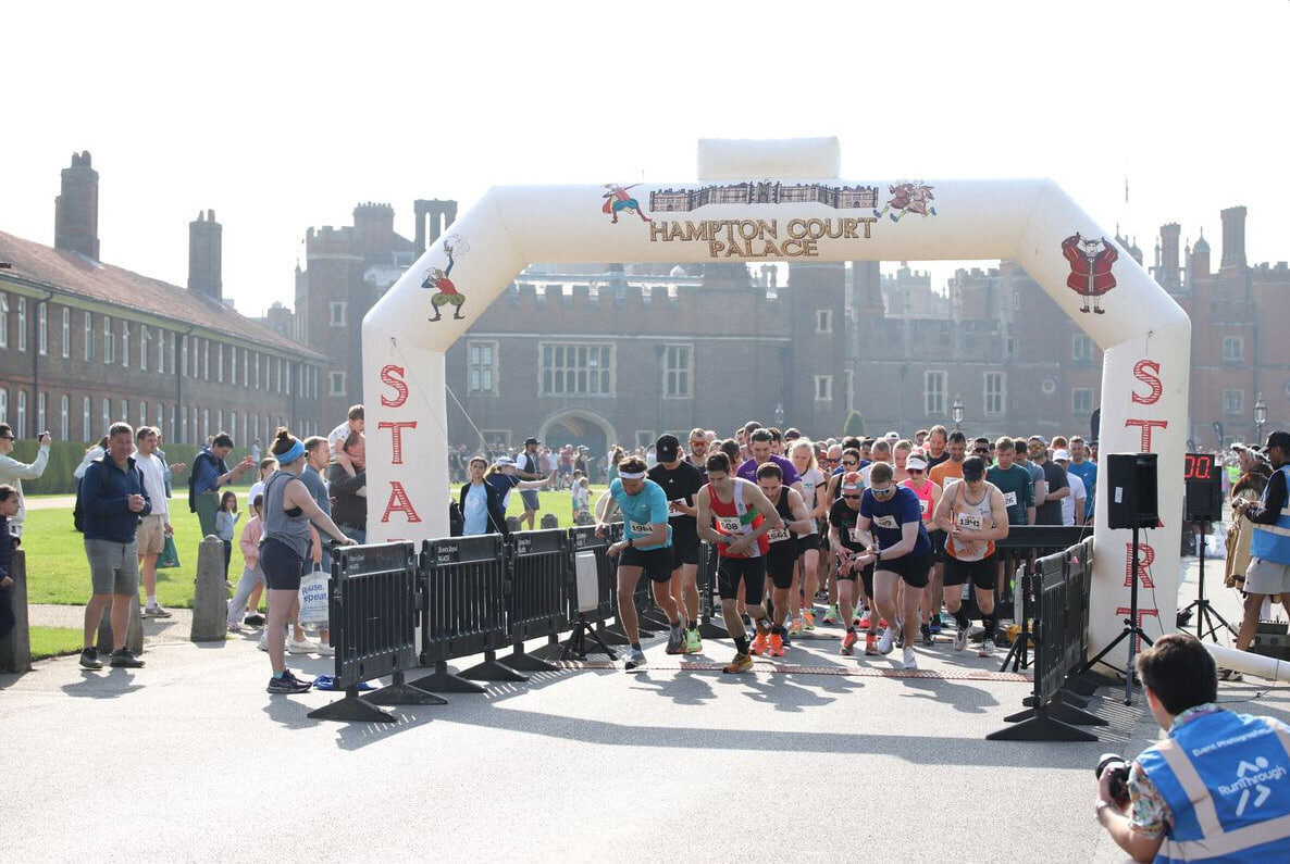 Runners at the starting line of the Hampton Court Palace 10K, with the historic palace in the background. The race begins under an inflatable arch labeled 